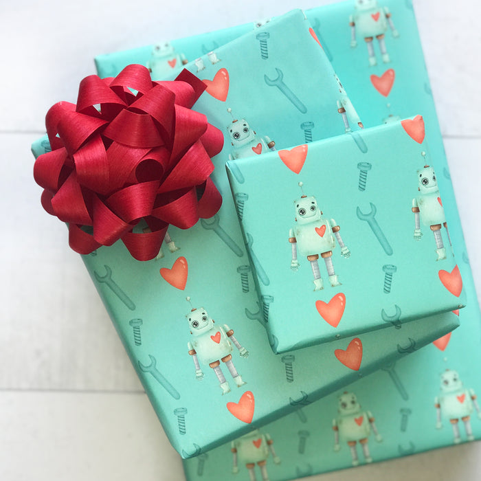 Three gifts wrapped in Waterleaf Paper Companys Dissolvable Gift Wrap, featuring robot, heart, and tool designs with a large red bow. Eco-friendly for septic systems.