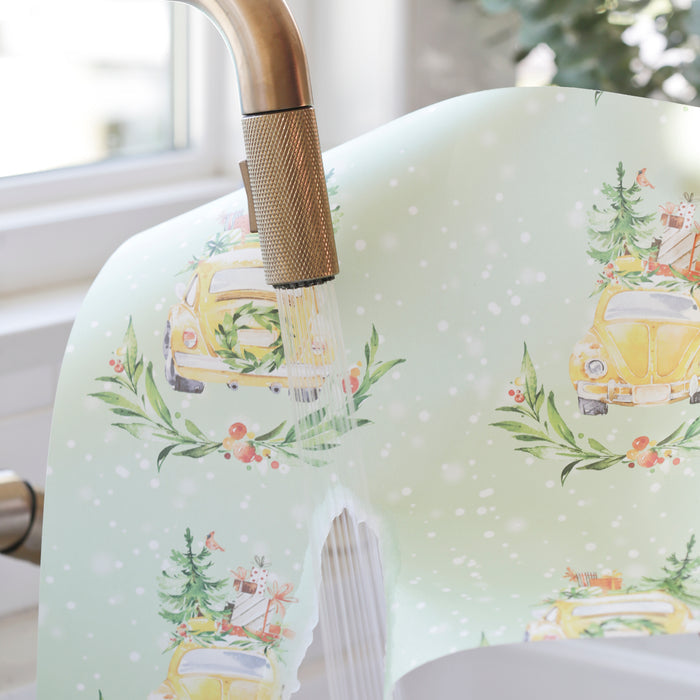 The Waterleaf Paper Companys Dissolvable Wrapping Paper showcases a yellow car adorned with Christmas trees and gifts beneath a brass faucet. Snowflake accents add to the festive vibe, and eco-manufacturing ensures your celebrations are environmentally friendly.