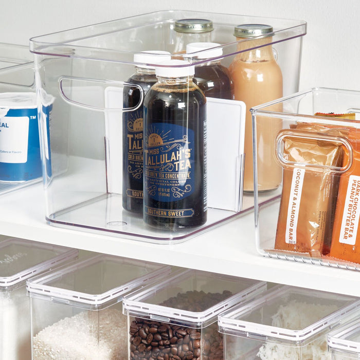 An organized pantry shelf features iDesigns BPA-free Divided Organizer Bin with Handles, made from recycled plastic. One bin neatly holds tea and juice bottles, another stores food packets, while additional containers with rice and beans ensure your kitchen storage remains neat and tidy.