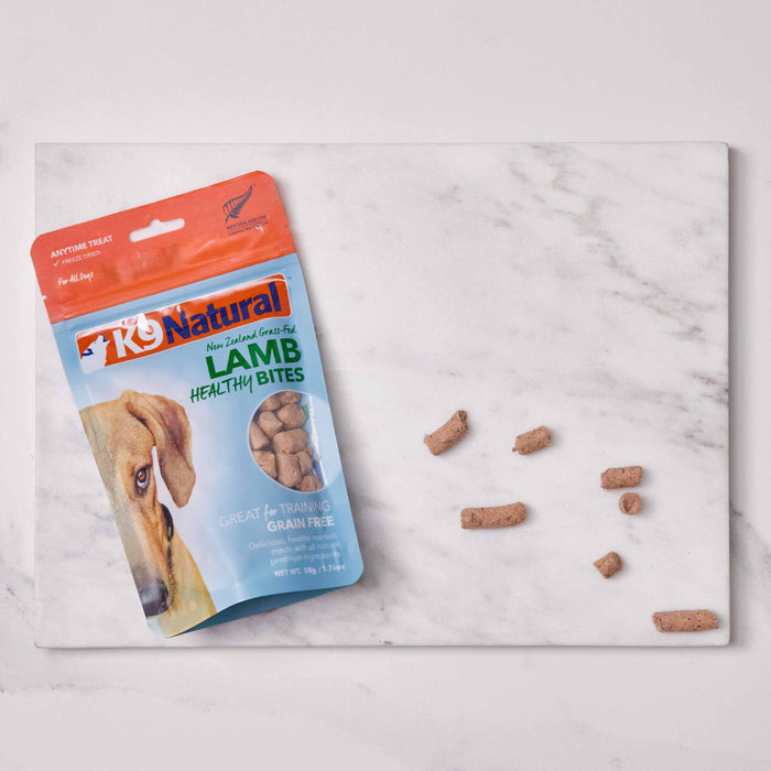 A package of K9 Natural Grain-Free Freeze-Dried Dog Treats lies on a marble surface, partially open with treats scattered nearby. The front features a dog image and the text Great for Training, Grain Free.