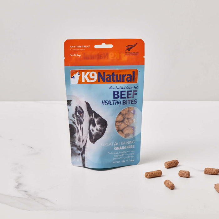 A package of K9 Natural Grain-Free Freeze-Dried Dog Treats, in orange and blue, rests on a white surface. This New Zealand product features a playful dog image with scattered brown bites, providing a natural snacking experience for your canine companion.