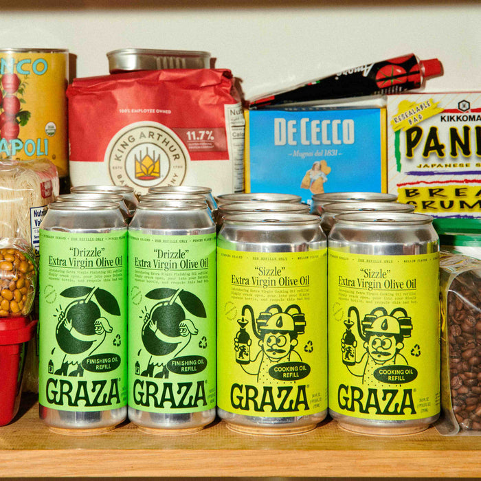 Grazas Drizzle Extra Virgin Olive Oil - Refill cans are nestled among pantry staples like flour, pasta, and beans on a rustic kitchen shelf. The scene exudes a warm, homey vibe with recyclable refills that make sustainable cooking stylish and convenient.
