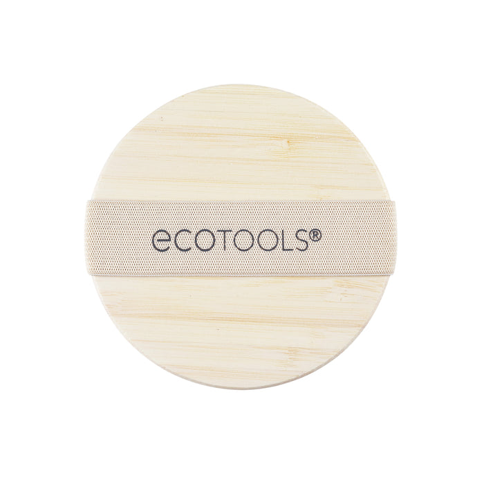 The EcoTools Dry Body Brush is a round, beige pad with a wooden texture and handle strap, made for skincare. Crafted from sustainable materials, it provides an eco-friendly exfoliating experience.