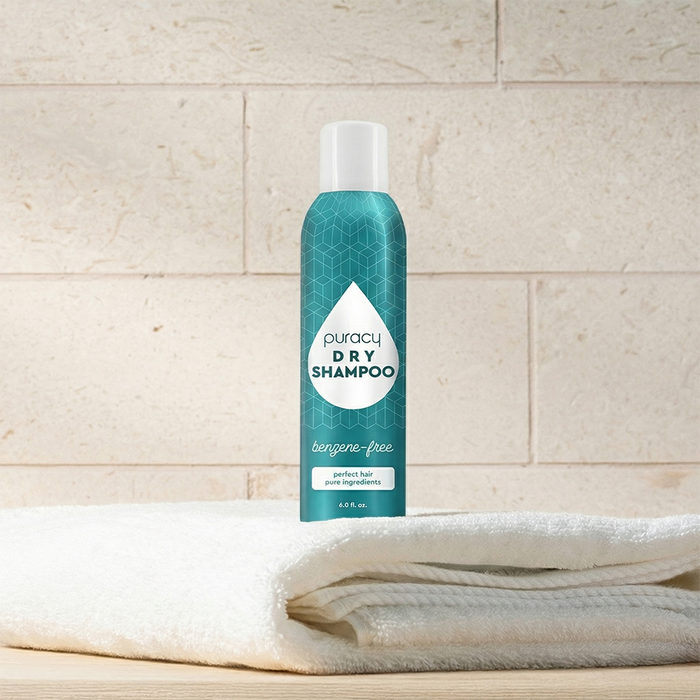 A blue can of Dry Shampoo (Benzene & Silicone-Free, Color-Safe) on white towels, beige tile backdrop.