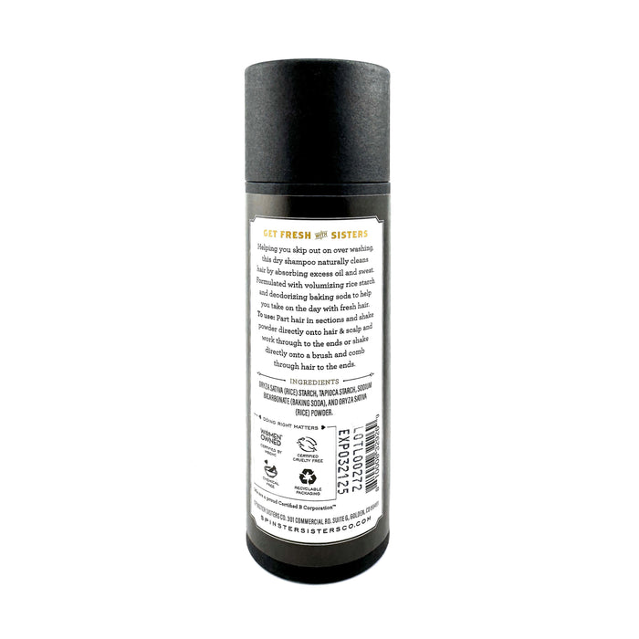 The Spinster Sisters Co. Dry Shampoo comes in a sleek black cylindrical container with a white label detailing ingredients and instructions. It features certification symbols and logos at the bottom. Infused with deodorizing baking soda for invigorating freshness, the design is completed by a black cap against a plain white background.