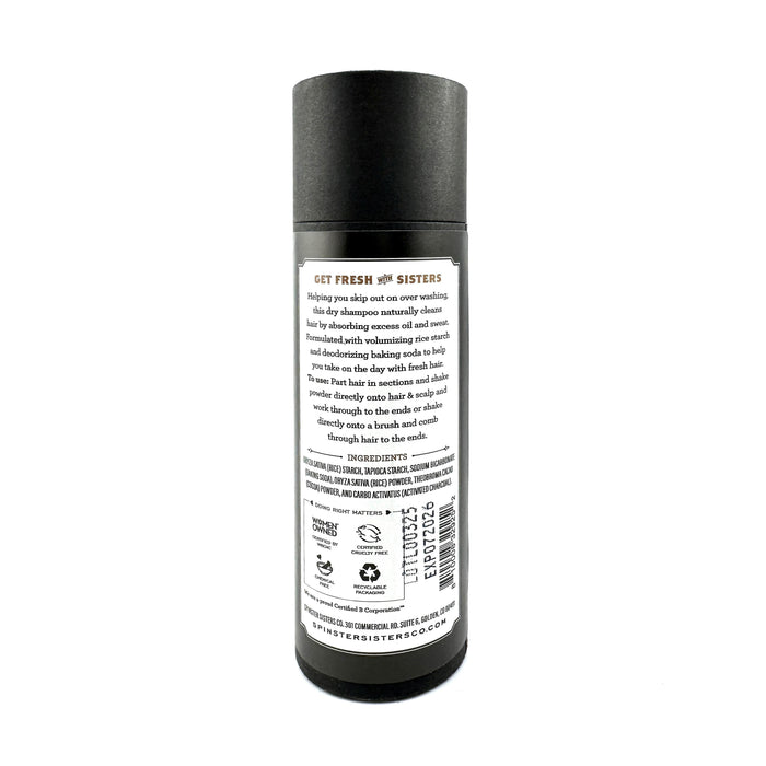 The Dry Shampoo by Spinster Sisters Co. comes in a sleek black cylindrical container with a white label showing instructions and ingredients, including deodorizing baking soda for freshness. A barcode and QR code are at the bottom for quick access to more product information.