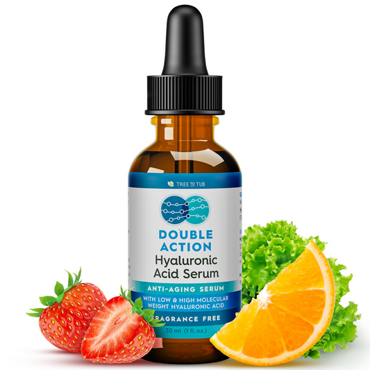 A bottle of Tree To Tubs Dual Action Deep Hydrating Hyaluronic Acid Serum with a dropper is placed among fresh strawberries, lettuce, and an orange slice. The label highlights it as a fragrance-free anti-aging serum for hydrated skin, with low and high molecular weight hyaluronic acid.