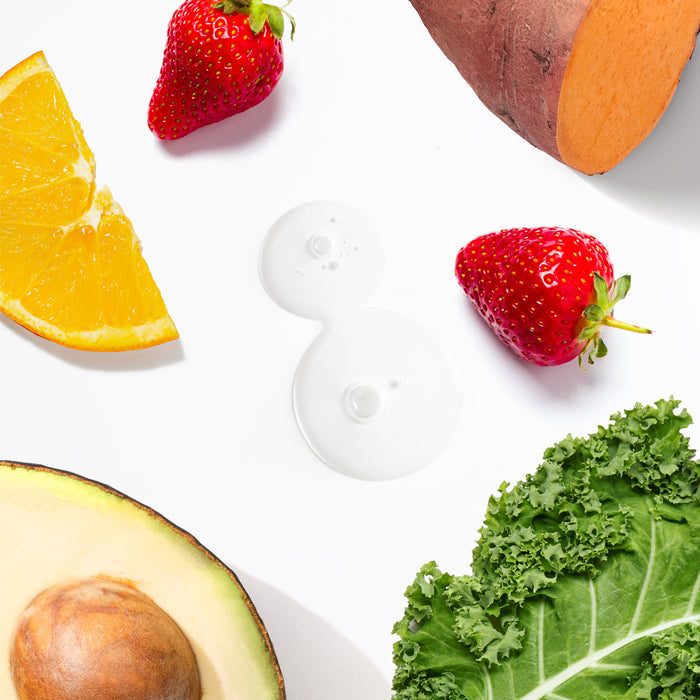 A flat lay image features sweet potato, strawberries, an orange slice, avocado, kale leaves, and two circles of Tree To Tubs Dual Action Deep Hydrating Hyaluronic Acid Serum for Face, showcasing fresh ingredients that inspire hydrated and rejuvenated skin.