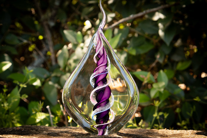 Dual memorial glass flame with two ashes spiraling around a purple core inside a clear teardrop vessel.