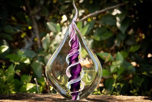 Dual memorial glass flame with two ashes spiraling around a purple core inside a clear teardrop vessel.