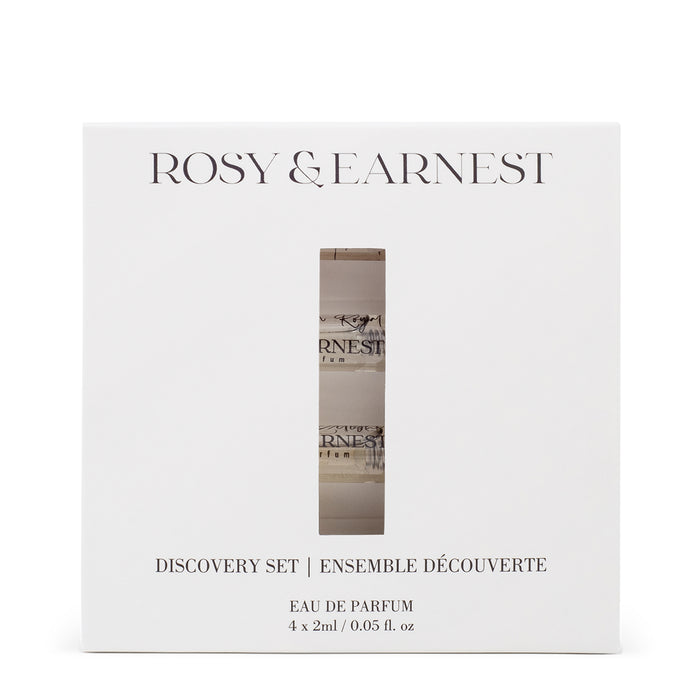 A white box labeled Rosy & Earnest with Discovery Set | Ensemble Découverte below, contains Eau de Parfum 4 x 2ml / 0.05 fl. oz. A vertical window reveals four small bottles, suggesting scents of vanilla and pistachio to explore.