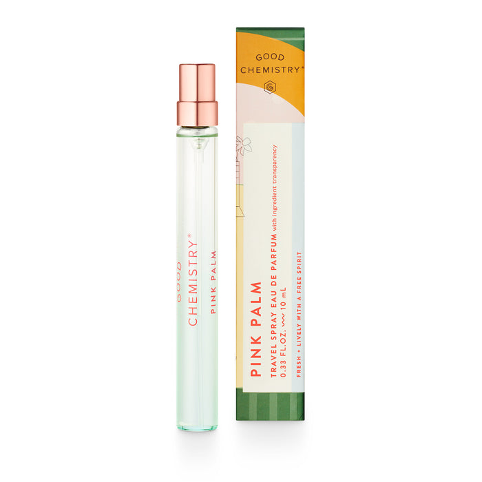 A slender, clear glass spray bottle of Good Chemistrys Eau De Parfum Travel Spray, Pink Palm, sits beside its colorful box with vibrant pink and green designs. The minimalist text bottle is part of a vegan and cruelty-free fragrance collection.