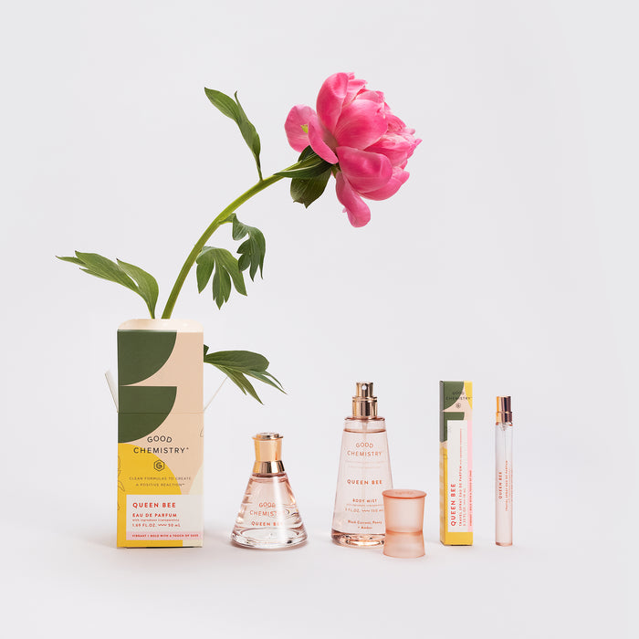 A collection of Good Chemistry Eau De Parfum bottles arranged in a row with a pink peony backdrop, showcasing boxed and unboxed vegan, cruelty-free perfume glass bottles and emphasizing the brands elegant packaging.
