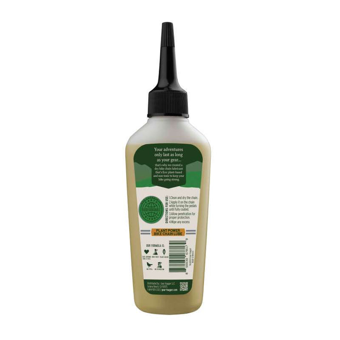 A green bottle with a black nozzle cap contains Gear Huggers Eco Dry Bike Lubricant, featuring a label with instructions and product information. The lubricant is non-toxic, bio-based, ideal for outdoors, and the back label highlights its eco-friendliness and sustainability.
