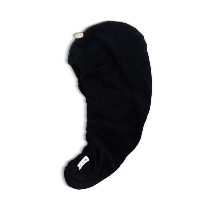The Kitsch Eco-Friendly Hair Towel, crafted from black fabric with a button closure, is ergonomically designed to wrap around wet hair. It features a white label on one side and promotes sustainable living.