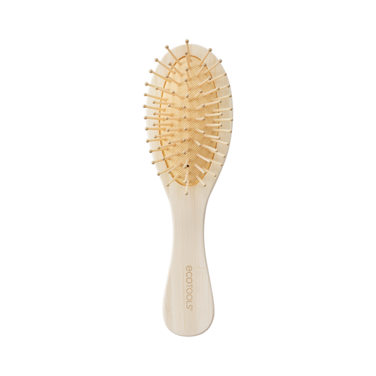 The EcoTools Eco Mini Shine Brush, crafted from 100% renewable bamboo in beige, features a curved handle and widely spaced bristles for gentle detangling. The handle displays the EcoTools logo, and the brush is elegantly showcased on a plain black background.