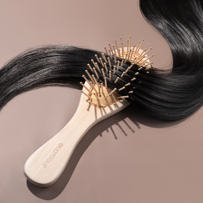 The EcoTools Eco Mini Shine Brush, crafted from 100% renewable bamboo, features fine bristles on a circular cushion with a polished handle. Its wooden design in light brown is accentuated by shiny black hair wrapped around the bristles.