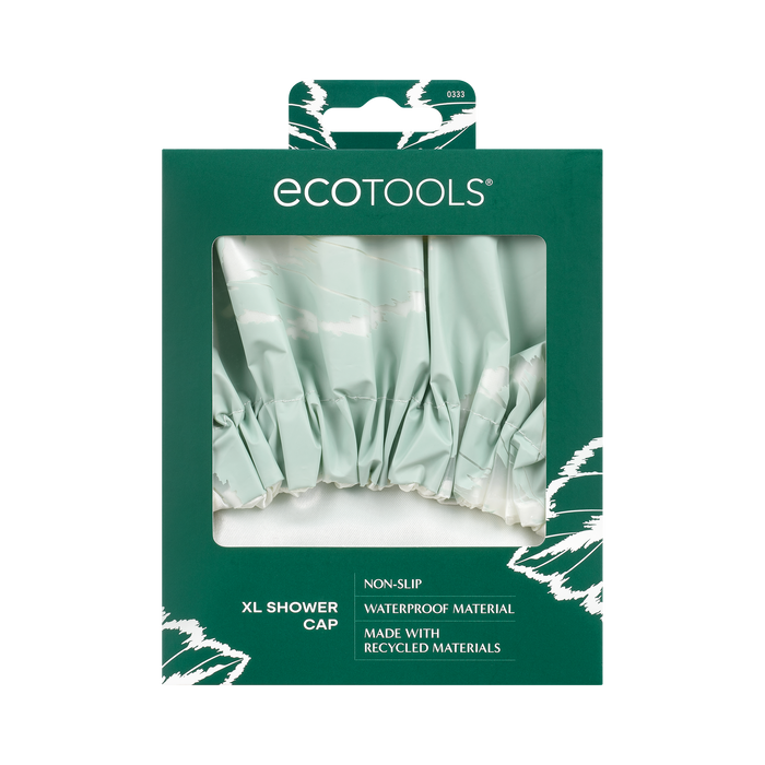 The EcoTools Eco XL Shower Cap packaging has a transparent window showing the reusable cap inside. It highlights its non-slip, waterproof design and sustainability while featuring white abstract designs for an eco-friendly appeal.
