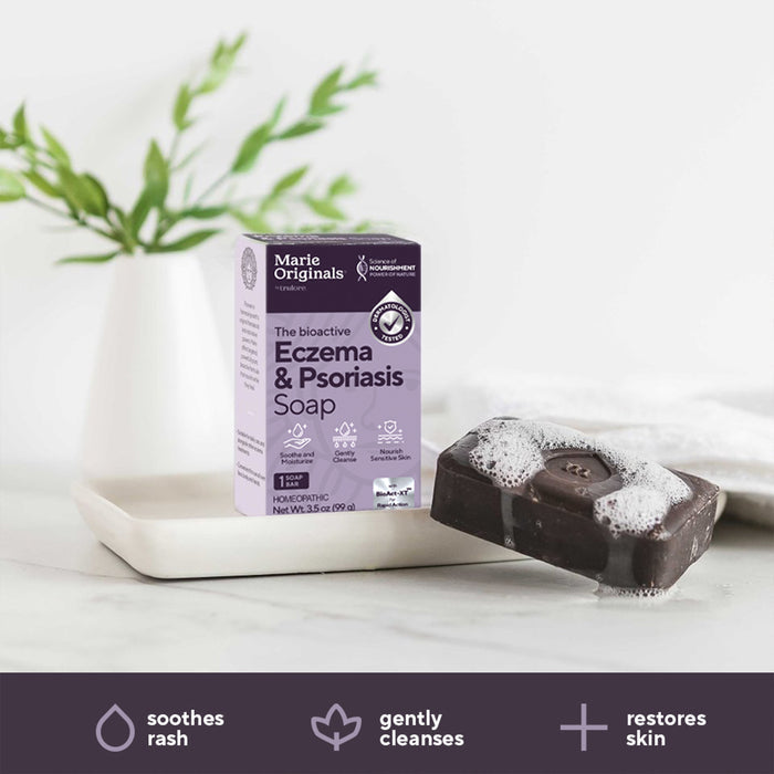 Marie Originals Eczema & Psoriasis Relief Soap sits by a foaming dark bar on a white dish with green leaves behind it. Three icons below show benefits: soothes rash, gently cleanses, and restores skin.