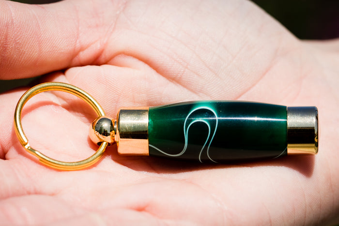 Emerald green acrylic keepsake urn pendant with white swirl pattern, gold end caps, and attached gold key ring.
