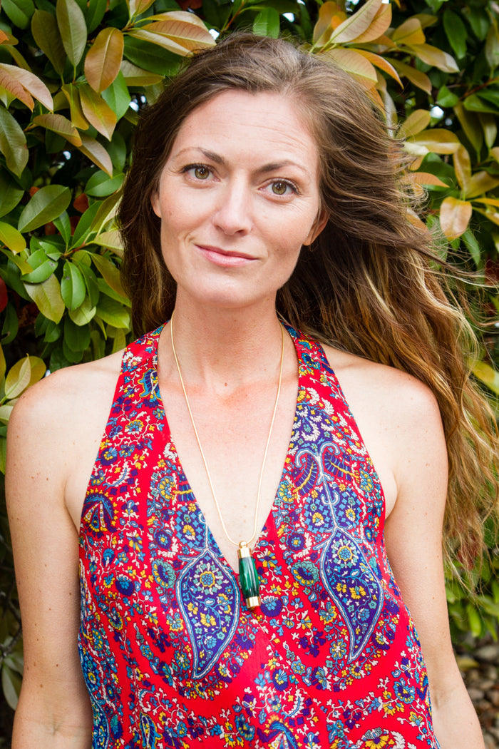 Model wearing an emerald green acrylic keepsake urn pendant on a gold chain against leafy backdrop