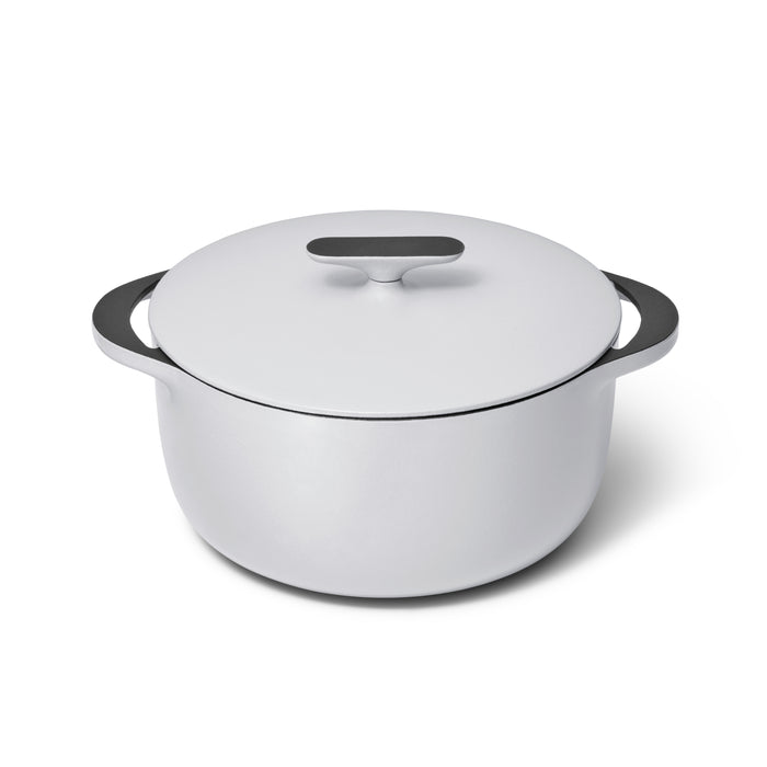 A Caraway Cast Iron Dutch Oven with a flat lid, 6.5 qt, featuring wide black handles and superior heat retention, sits on a plain background. It boasts a sleek, modern design in round white enameled cast iron.