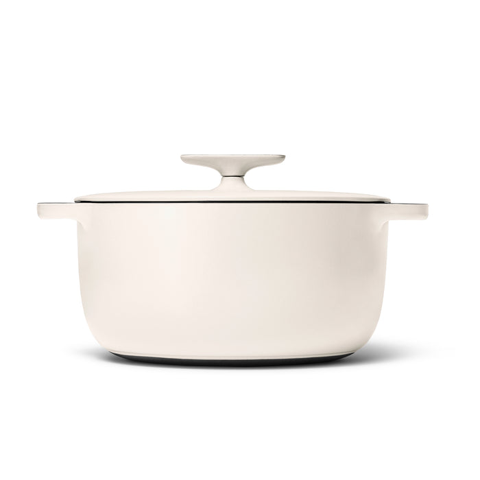 The Caraway Cast Iron Dutch Oven with Flat Lid, 6.5 qt, is cream-colored and round with wide handles. It features superior heat retention, a smooth finish, a lid knob, and comes in white.
