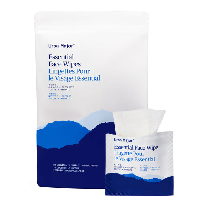 A package and a single packet of Ursa Major Essential Face Wipes, individually wrapped, feature blue mountain graphics and bilingual English-French text highlighting their 4-in-1 cleansing, exfoliating, soothing, and hydrating benefits.