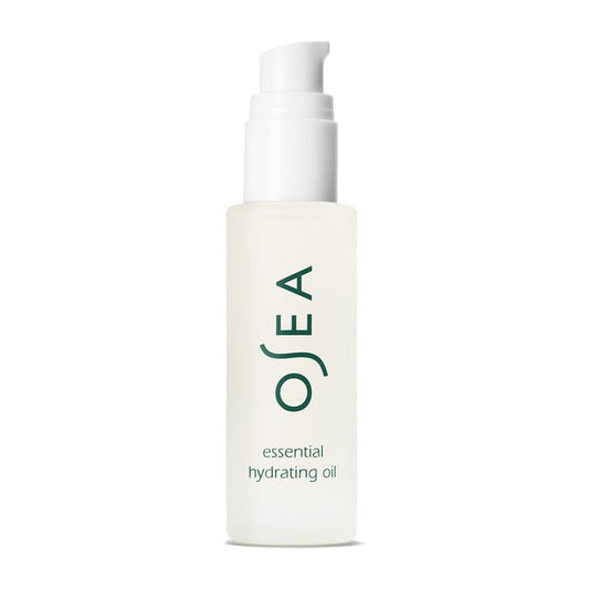 A clear bottle of OSEA Essential Hydrating Oil with a white pump promises a glowing complexion. OSEA is printed vertically in green, above smaller text reading essential hydrating oil, all set against a plain white background.
