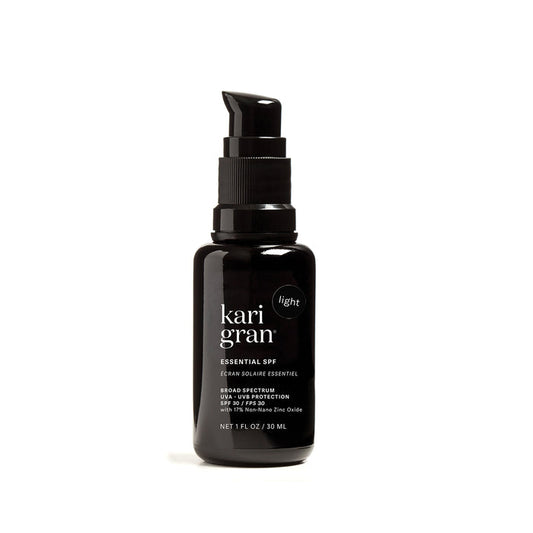 A black pump bottle labeled Kari Gran Essential Tinted SPF 30 contains a mineral sunscreen offering broad-spectrum UVA/UVB protection and 15% non-nano zinc oxide, infused with red raspberry seed oil. It provides light coverage in a NET 1 FL OZ / 30 ML size.