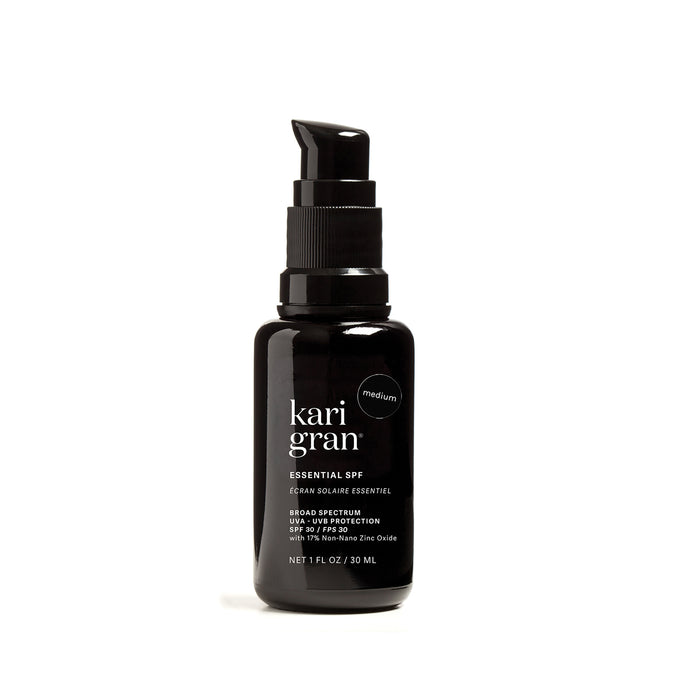The Kari Gran Essential Tinted SPF 30 sunscreen features broad spectrum UVA/UVB protection with 15% non-nano zinc oxide. This black bottle, equipped with a pump dispenser, contains a 1 fl oz medium shade tinted mineral formula enhanced with red raspberry seed oil for nourishment.