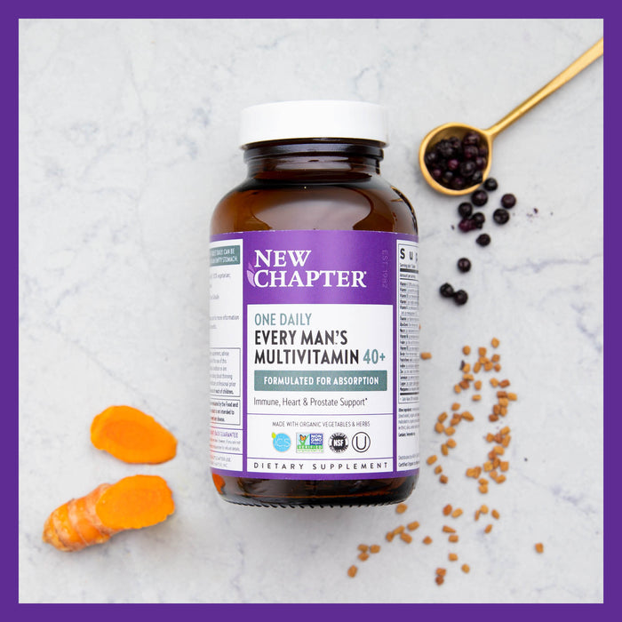 New Chapters Every Man™s One Daily 40+ bottle with a purple label rests on a marble surface, surrounded by turmeric slices, black berries in a spoon, and scattered seeds, highlighting this whole-food fermented multivitamin for men over 40.