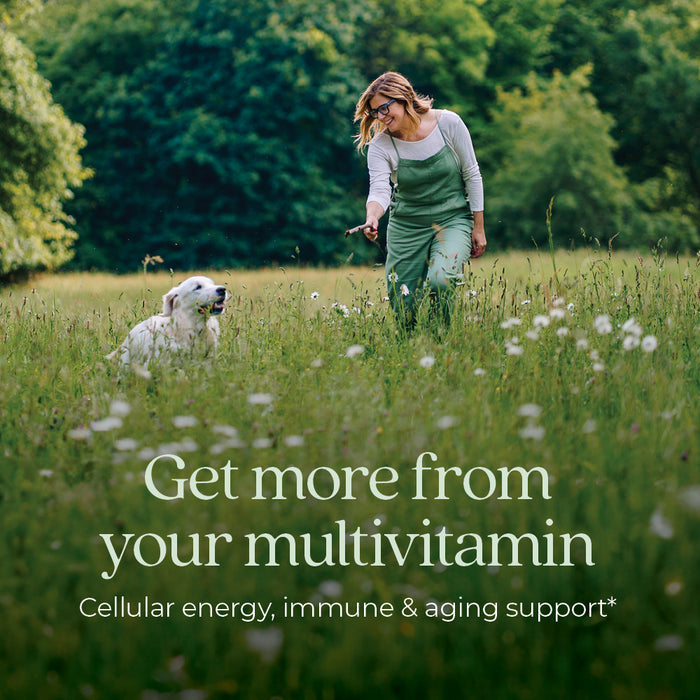 A person wearing overalls walks through a grassy field with a dog. Text on the image reads, "Get more from your multivitamin. Cellular energy, immune &amp; aging support." Lush greenery surrounds them under a clear sky.