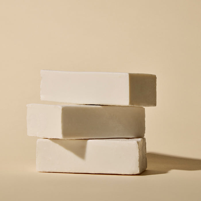 Three rectangular white Phil's Everything Bar soaps, enriched with chia seed oil, are stacked unevenly on a beige surface against a matching background, casting soft shadows to the right.