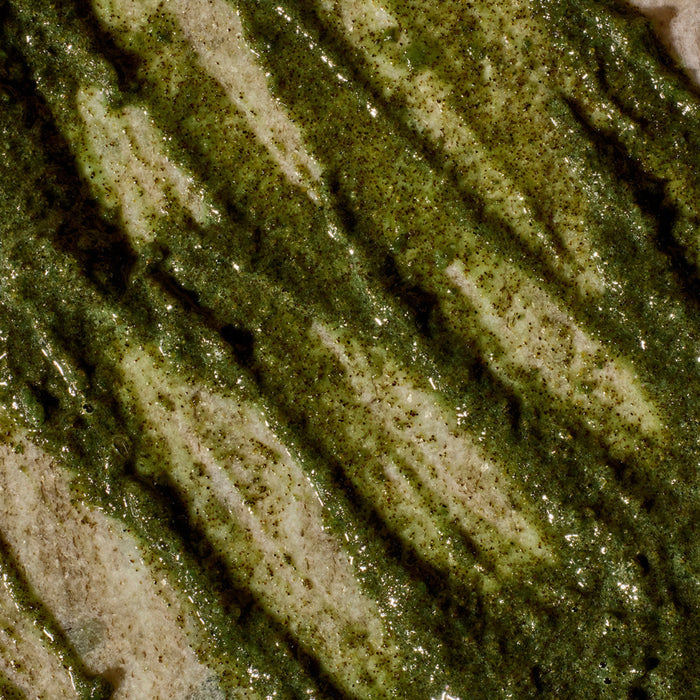 Close-up of Phil's Exfoliating Facial Cleanser by showing its glossy, speckled, and creamy texture with diagonal streaks of green on a pale base, highlighting the product’s textured surface.