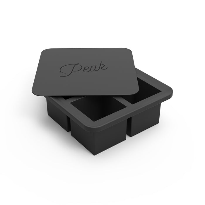 A black W&P Extra Large Ice Cube Tray with four oversized square compartments and a slightly open lid reveals the interior. Designed for slow melting ice, it sits elegantly against a plain white background.