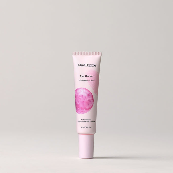 A tube of Mad Hippie Eye Cream, featuring a pink circle design, stands upright against a light gray background. Its rich in peptides and antioxidants, with text highlighting its ingredients, and supports their recycling program for sustainable beauty choices.