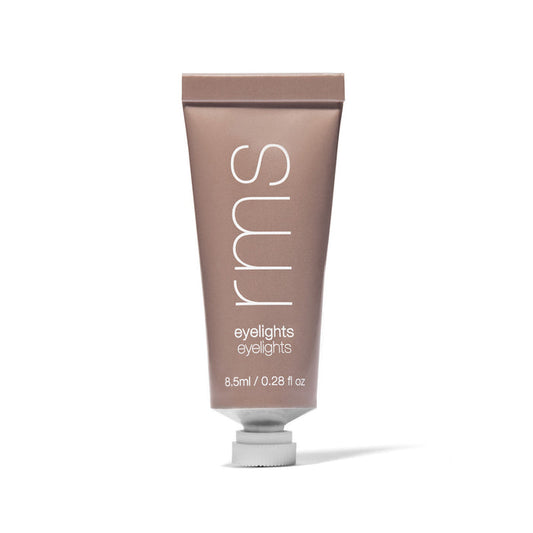 A metallic RMS Eyelights Cream Eyeshadow tube stands upright on a white background, featuring a bronze finish. The RMS logo is printed in white above Eyelights, highlighting the allure of cream eyeshadows made with organic extracts in captivating metallic shades.