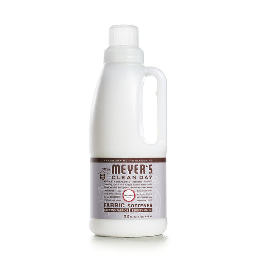 A white 32 fl oz Mrs. Meyers Fabric Softener bottle, featuring a side handle and brown label with white text, showcases its essential oil blend for softening fabrics and reducing static.