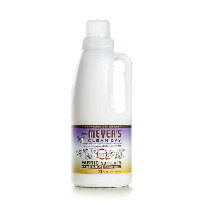 Mrs. Meyers Fabric Softener, 32 fl oz (946 ml), features a handle and essential oils. Its label showcases benefits and natural ingredients on a white and purple background with floral designs.