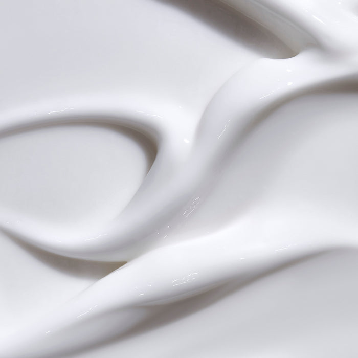 Close-up of The Honest Companys Face + Body Lotion, showcasing a silky, flowing white liquid texture with subtle highlights. Crafted for all skin types using naturally derived ingredients, its gentle wave-like appearance exudes luxury.