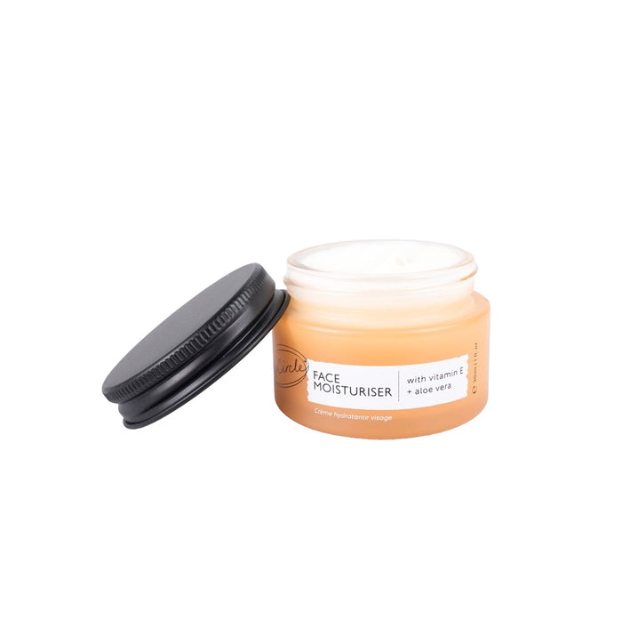 An open orange jar of UpCircles Face Moisturizer with Vitamin E + Aloe Vera shows its creamy contents. The moisturizing formula is enriched with brightening ingredients like vitamin E and aloe vera.