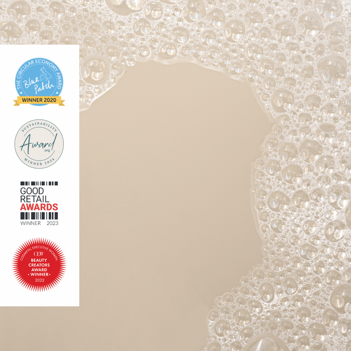 Cluster of small soap bubbles creating an open space in the center with award logos displayed on the left side. The logos include various awards for sustainability, retail, and beauty. The background is beige.