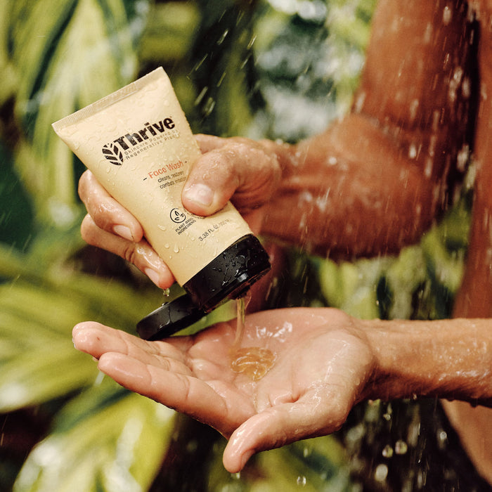 Hands squeeze Thrive Natural Care Face Wash into the palm, with a blurred nature backdrop. The open cap lets the natural formula emerge, framed by greenery and regenerative plant ingredients, for a fresh and invigorating feel.