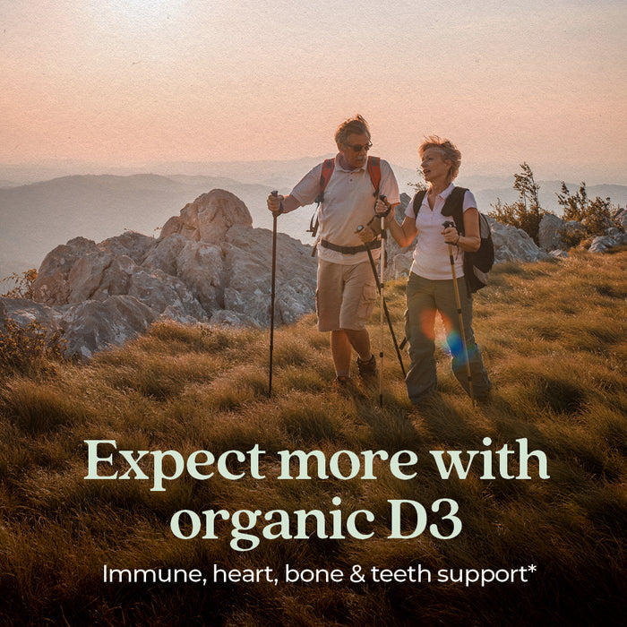 A man and woman hike with trekking poles on a grassy mountain at sunset. Text reads: Expect more with New Chapter Fermented Vitamin D3, 2,000 IU—for immune, heart & bone support.*.