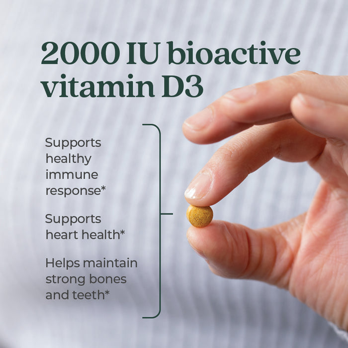 A hand holds a small Fermented Vitamin D3 tablet by New Chapter. Text reads: 2,000 IU for immune, heart & bone support to help maintain strong bones and teeth.