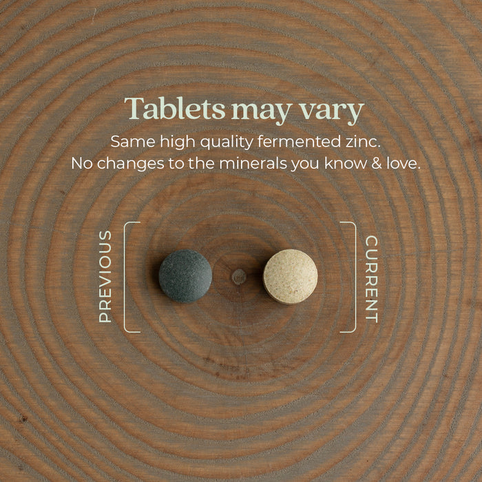 Two tablets on a wooden surface. The left tablet is dark and labeled "Previous," while the right tablet is light and labeled "Current." Text above reads: "Tablets may vary. Same high quality fermented zinc. No changes to the minerals you know &amp; love.