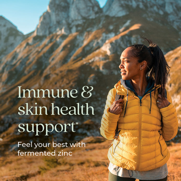 A person in a yellow jacket and backpack stands outdoors with mountains in the background. The text reads "Immune &amp; skin health support* Feel your best with fermented zinc.