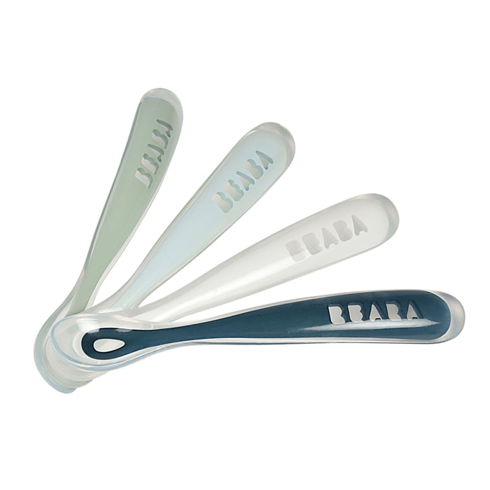 A set of four BEABA First Foods Silicone Spoons, in green and blue tones, are arranged fan-like. The translucent handles feature the BEABA brand name, ideal for introducing solids.