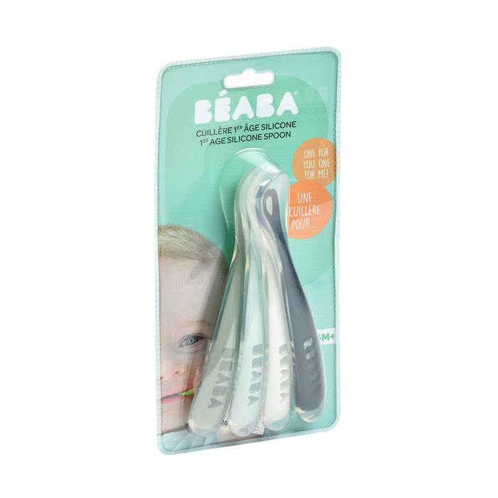 The BEABA First Foods Silicone Spoons set contains four baby spoons in white, light blue, and gray with a childs face design, perfect for infant feeding.
